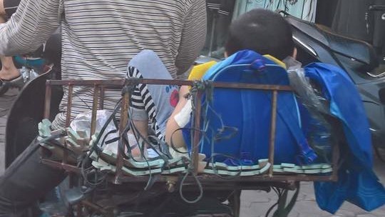 Bố chở con nằm trong khung sắt tự chế đến trường
